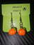 Halloween pumpkin earrings with orange pumpkin charms, green bead accents, and metal hooks, displayed on a Dnaasty Crafts card