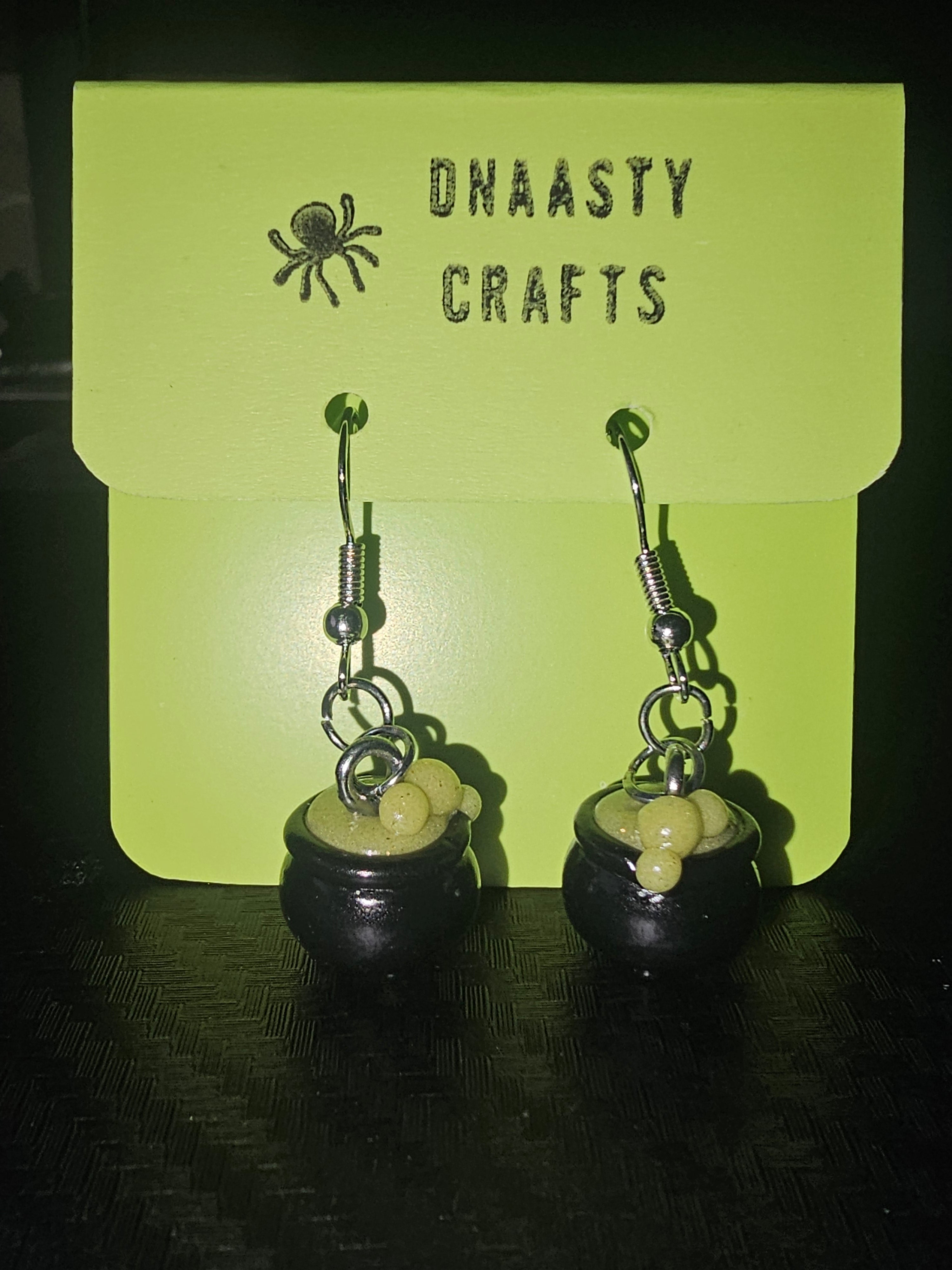 Handmade witch cauldron earrings with yellow beads and silver hooks displayed on a green card with black text and spider illustration