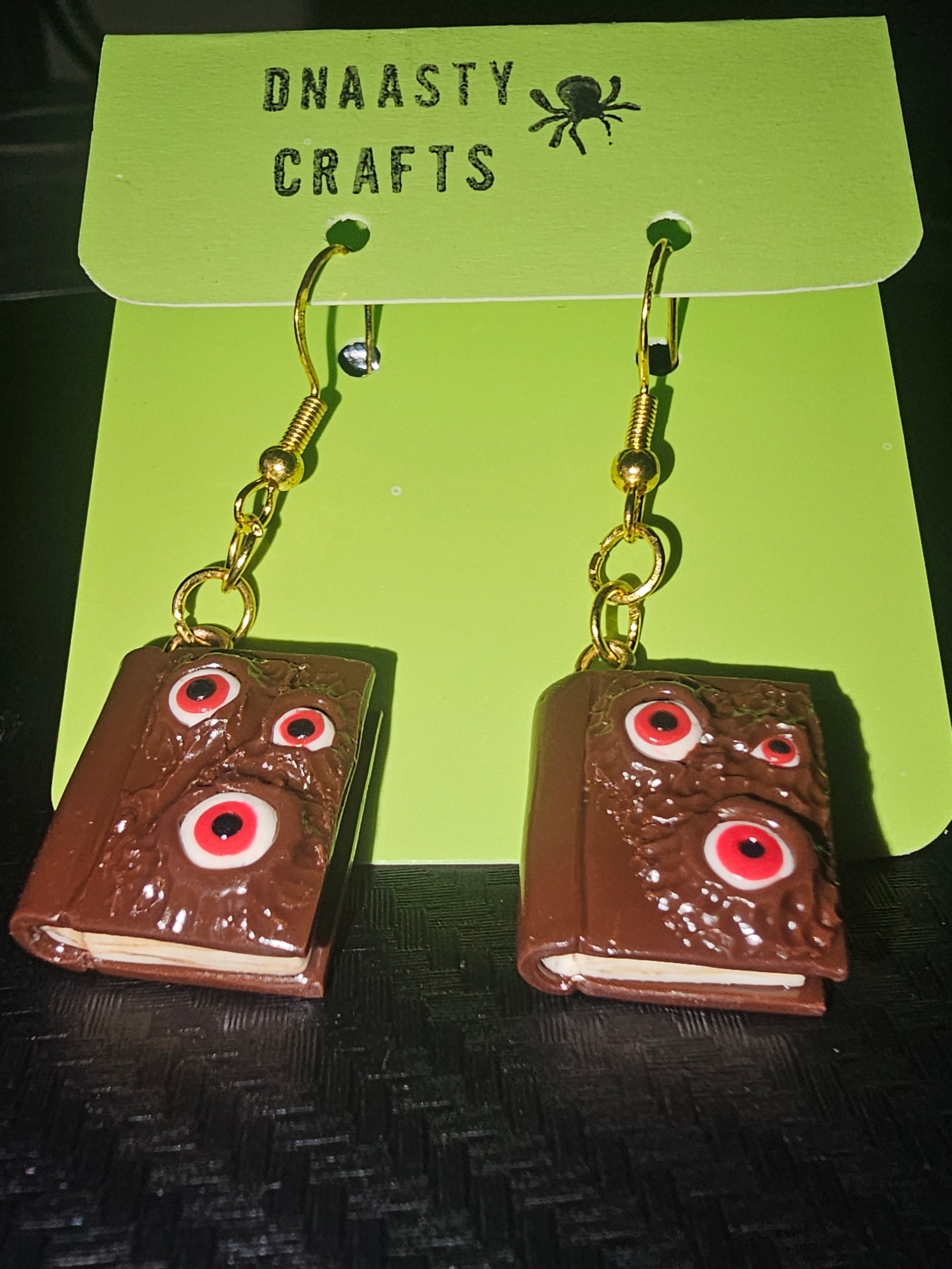 Necronomicon Book of the Dead earrings with brown textured polymer clay and red eye designs, hanging from gold hooks, gothic style jewelry