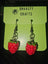 Red and green strawberry-shaped earrings made of glossy polymer clay with metal hooks, displayed on a green Dnaasty Crafts card