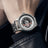 Black men's luxury automatic mechanical watch with a round dial, intricate skeleton design, stainless steel strap, and modern style