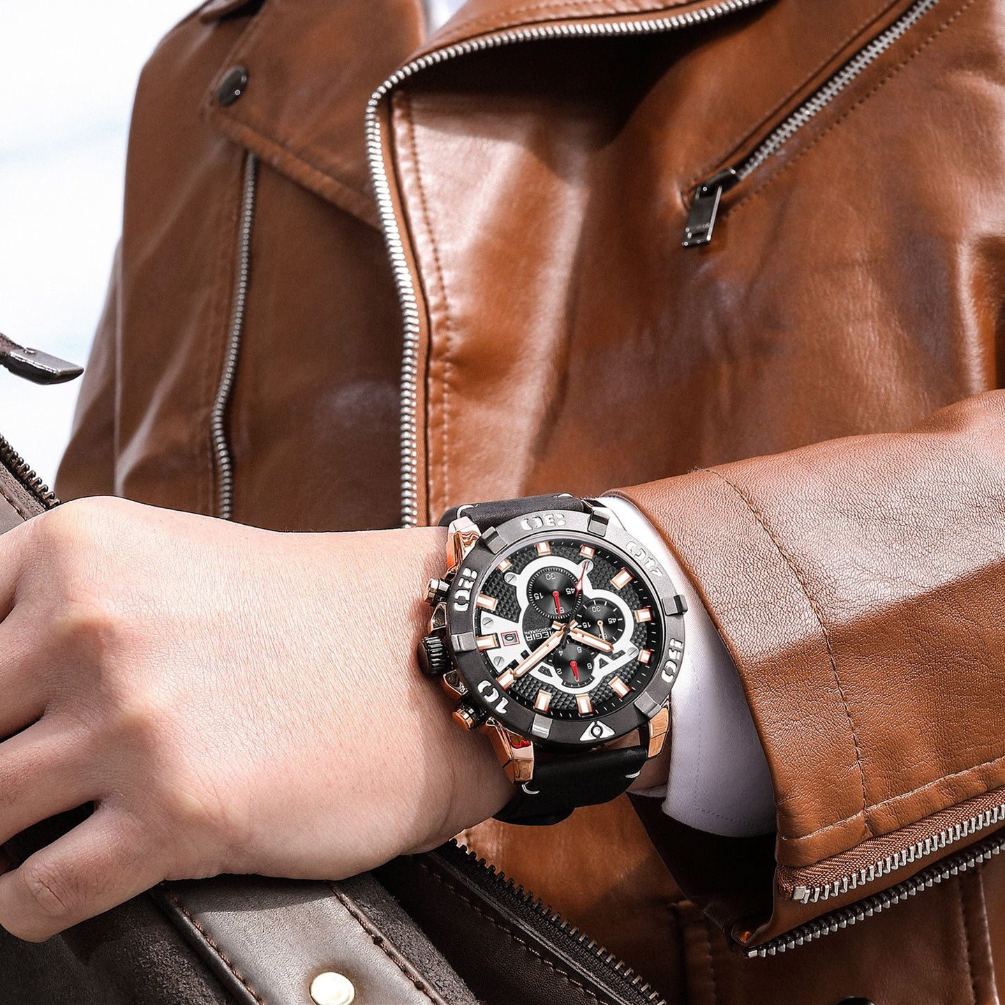 Luxury men's chronograph sports watch with large black dial, rose gold accents, and black silicone strap on a man's wrist, brown leather jacket in background