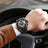 Luxury men's chronograph sports watch with large 48.5mm black bezel, black leather strap, rose gold case, and detailed dial with subdials and date window