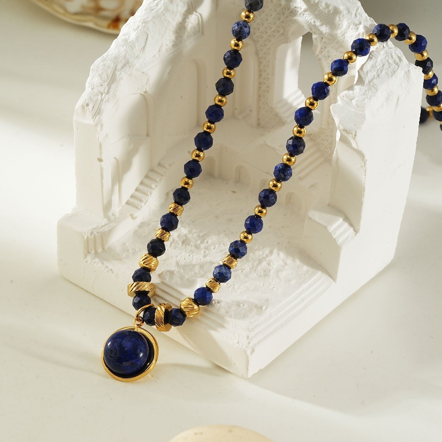 Elegant beaded necklace featuring deep blue lapis lazuli stones and gold accents with a round lapis lazuli pendant, perfect for sophisticated style.