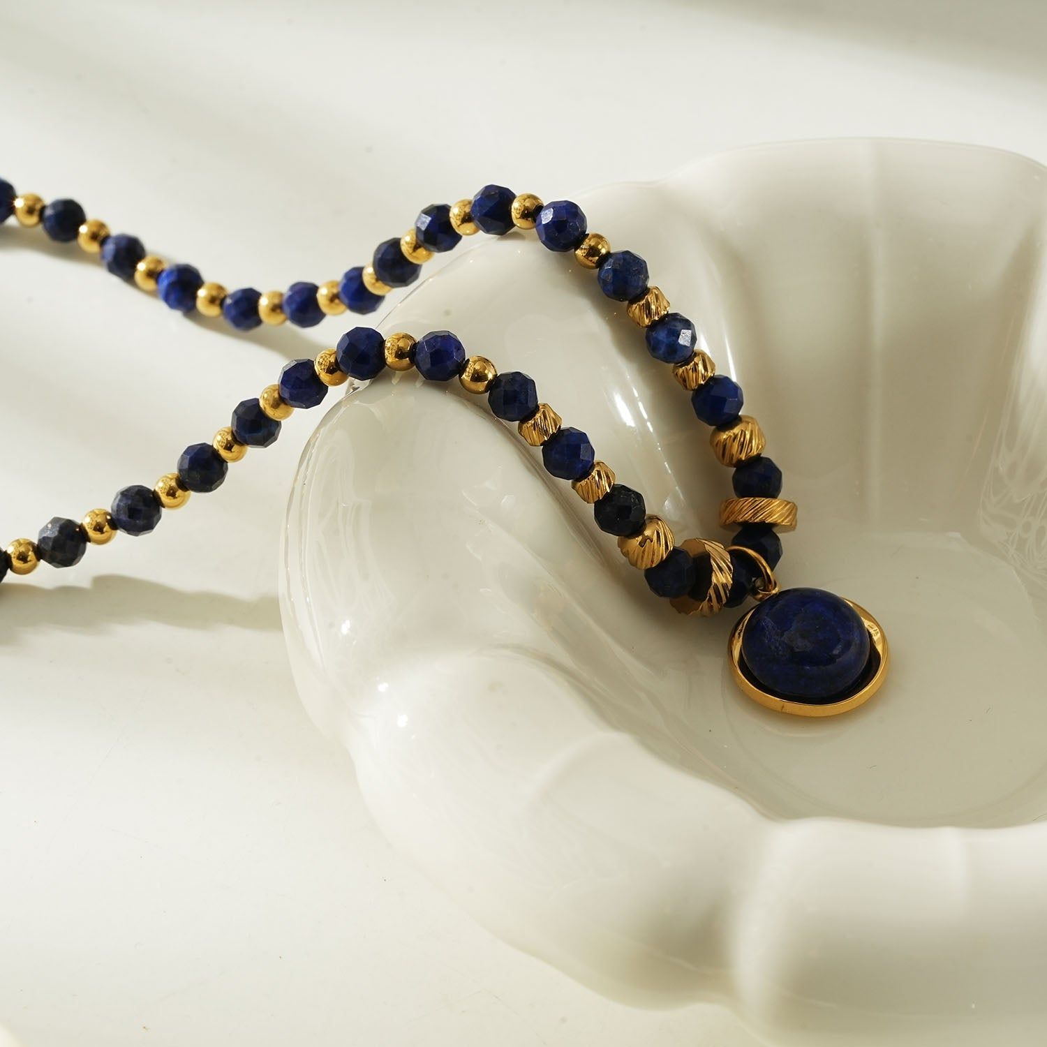Elegant beaded necklace featuring deep blue lapis lazuli stones and gold accents with a round lapis lazuli pendant, perfect for sophisticated style.