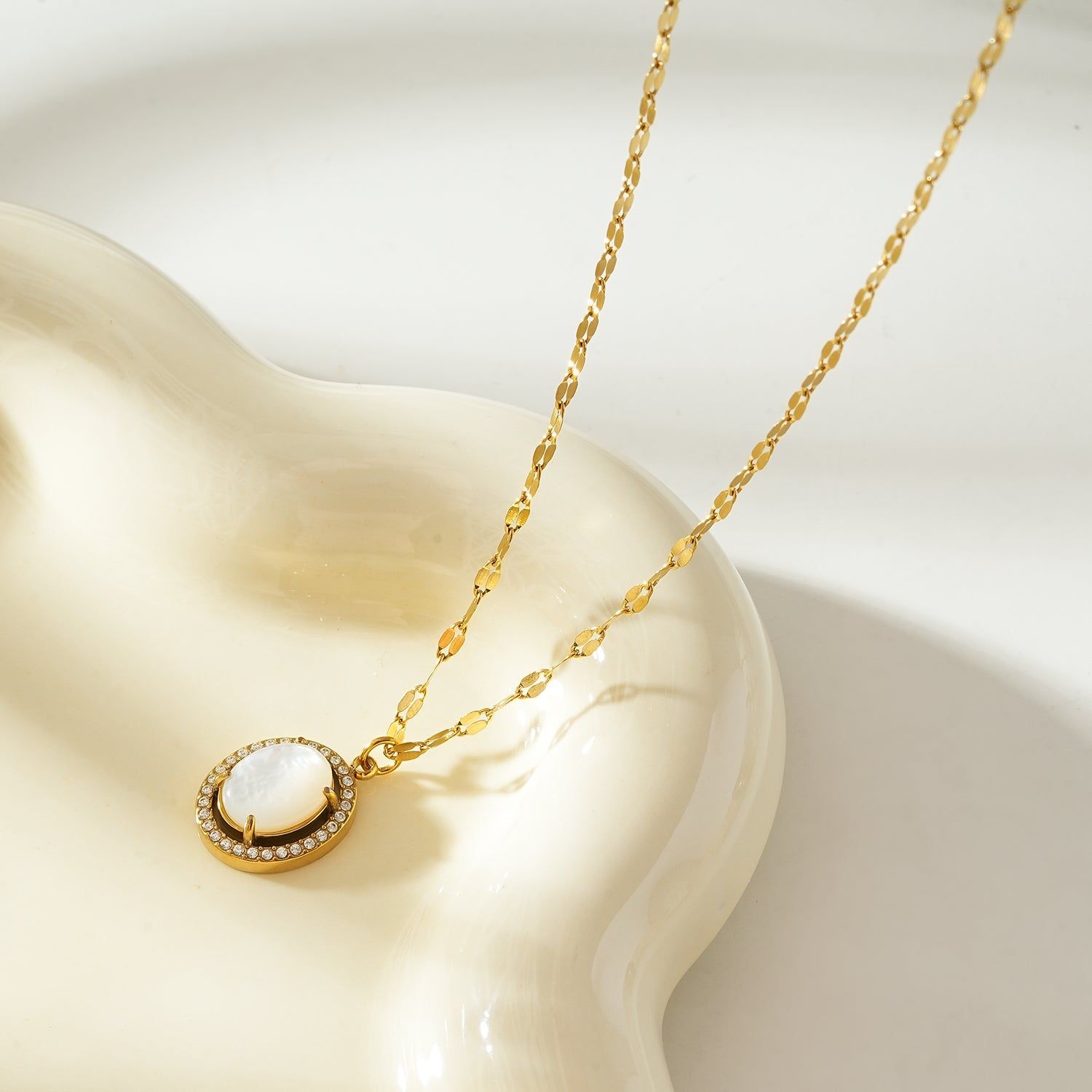 Gold pendant necklace with a freshwater pearl center, surrounded by a halo of sparkling zirconia stones, on a delicate gold chain