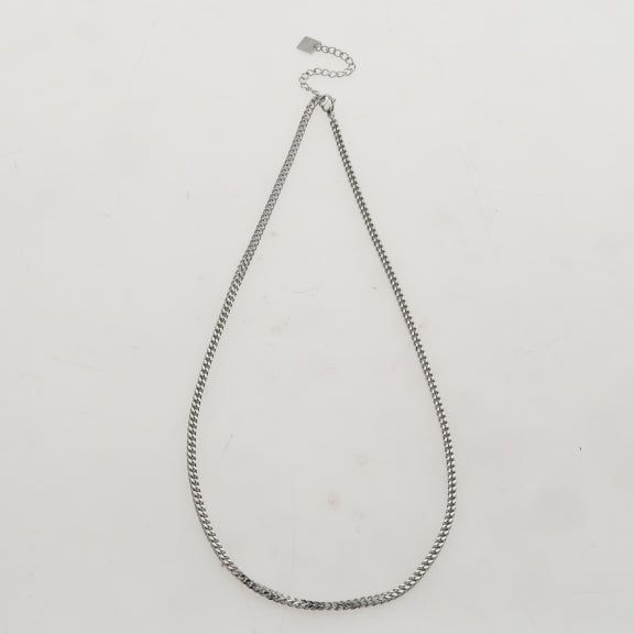 Silver Cuban link chain necklace on a male model with dark hair, wearing a black t-shirt, close-up shot, sleek and stylish jewelry