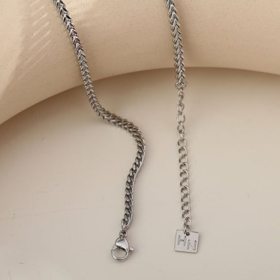 Silver Cuban link chain necklace on a male model with dark hair, wearing a black t-shirt, close-up shot, sleek and stylish jewelry