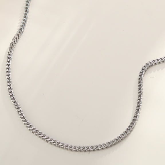 Silver Cuban link chain necklace on a male model with dark hair, wearing a black t-shirt, close-up shot, sleek and stylish jewelry