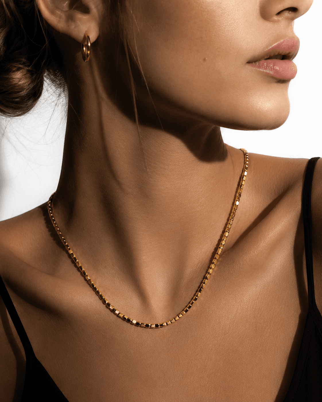 Gold beaded dainty chain necklace with small square beads, resting on a decorative ceramic dish with a scalloped edge, ideal for layering or everyday wear