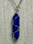 Silver chain necklace with a wire-wrapped deep blue gemstone pendant, set against a textured fabric background